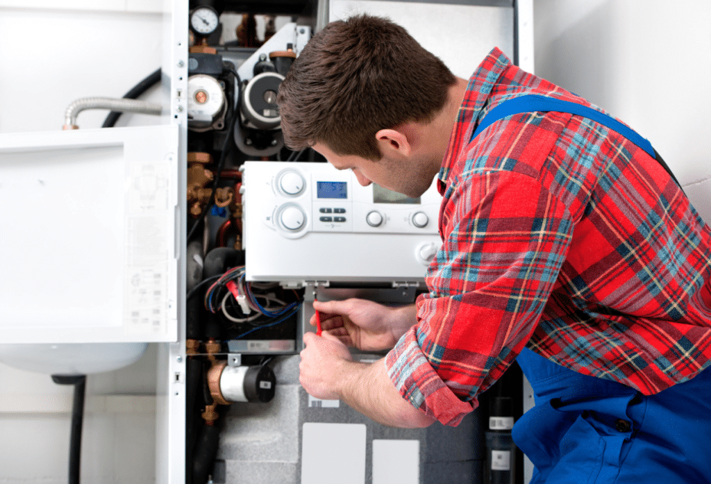 Technician servicing a wall-mounted boiler system with the front panel open during maintenance.